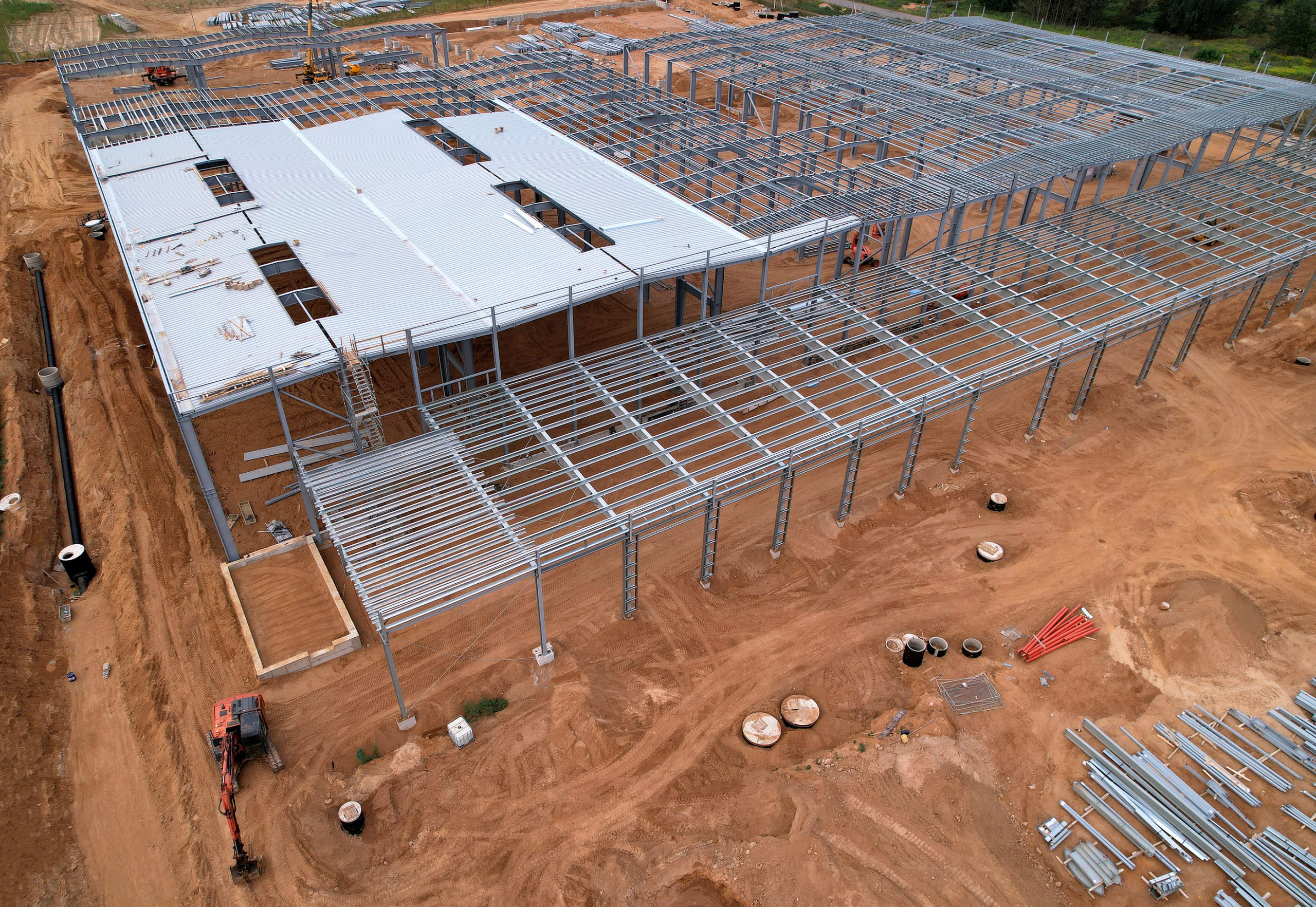 Construction of warehouse from metal structures. Industrial building on light gauge steel framing. Frame of modern hangar or factory. Aerial view of a construction site with steel structure warehouse.